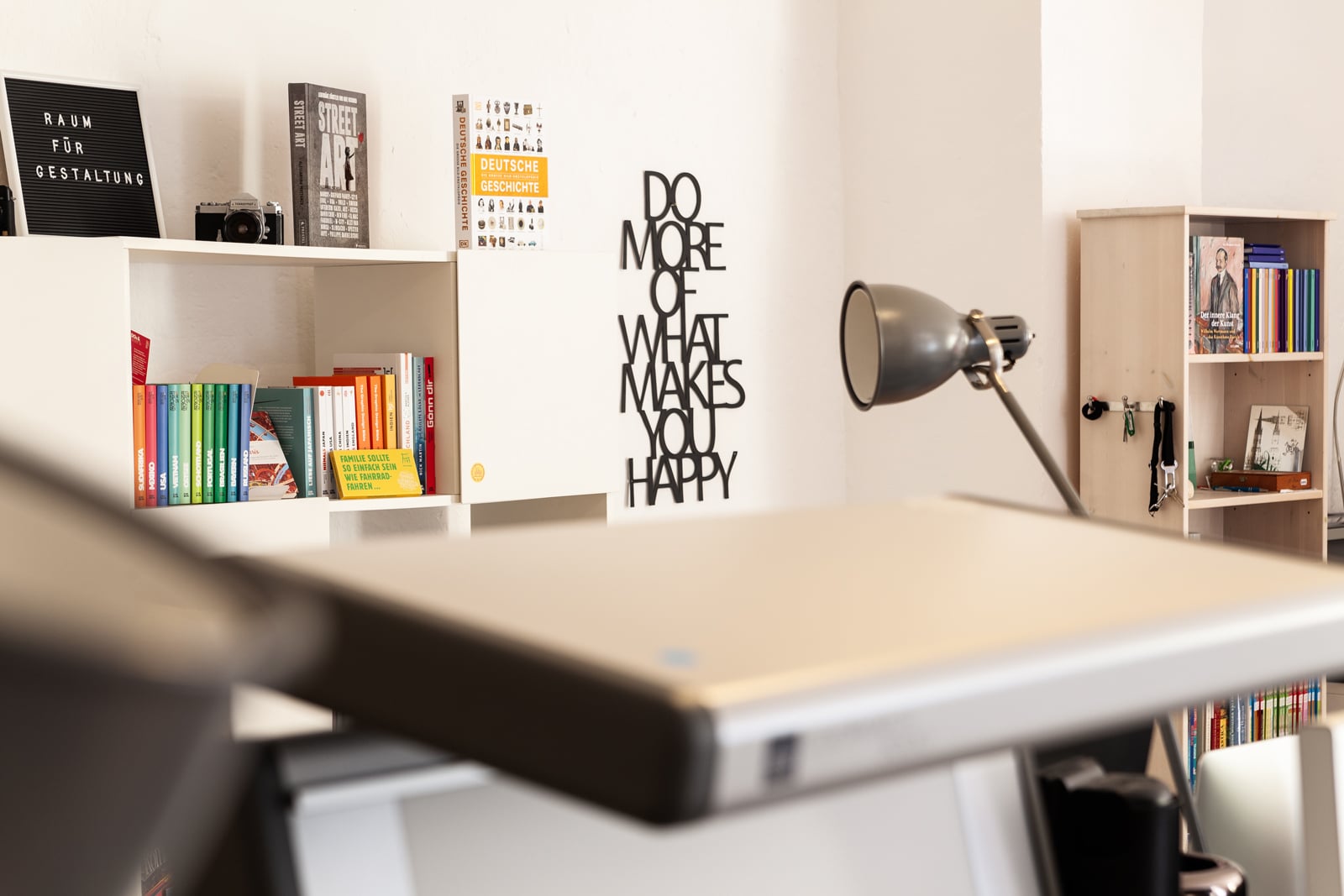 REMOTE ARBEITEN VERBUNDEN SEIN UND BLEIBEN, gezeigt wird eine Innenaufnahme des Büros von Weiß Freiburg, im Vordergrund ist Unschärfe technisches Equipment zur Buchproduktion zu sehen, im Hintergrund einige Bücher aus dem Portfolio der Agentur